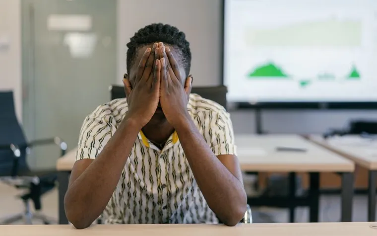 An office worker sitting at a meeting room desk with both hands over their face