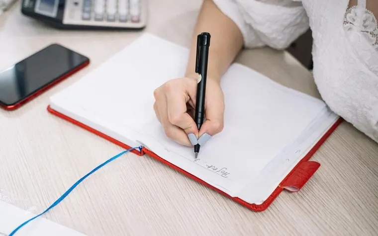 A hand writing notes in a notebook with a pen