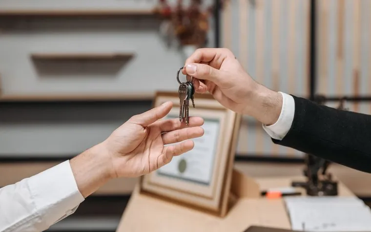 A hand receiving keys at a property office beside a framed certificate