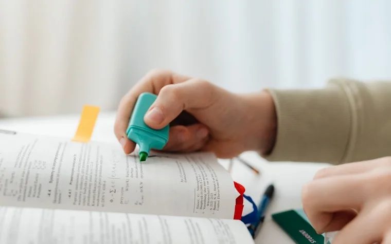 A hand marking a line of text in a book with a highlighter