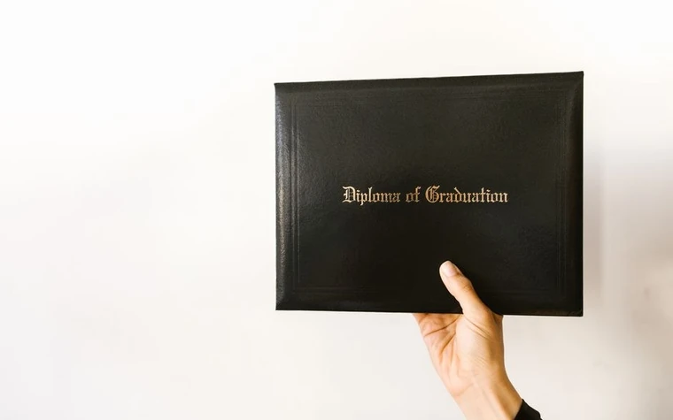 A hand holding a diploma folder